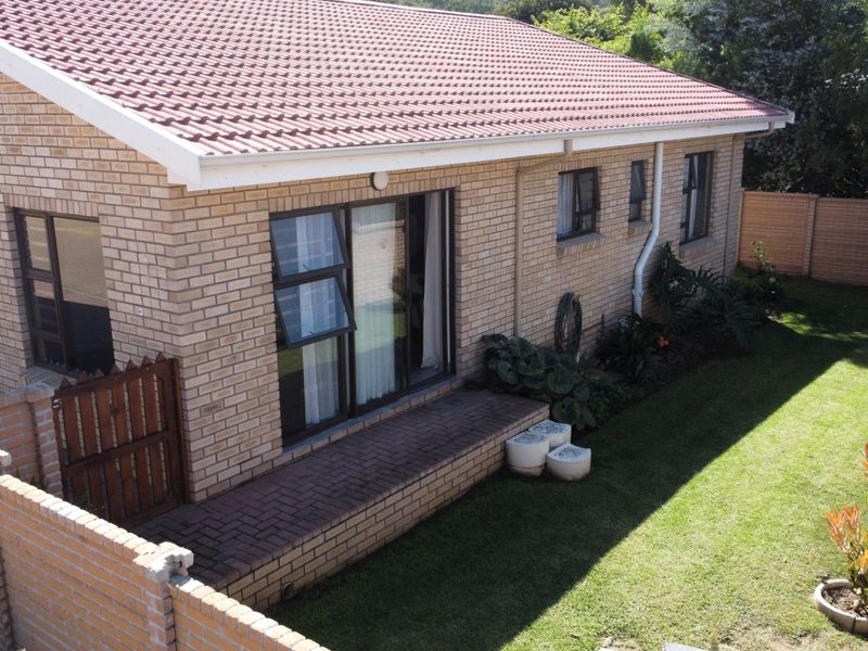 Rear view of a brick-faced house featuring a tiled roof, paved patio area, and a well-maintained garden with boundary walling.