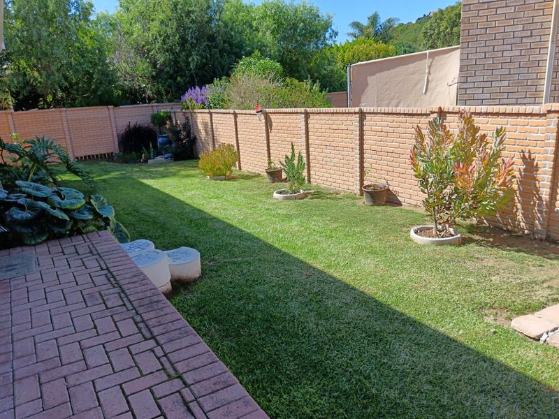 A well-maintained private garden featuring a paved patio area, lush green lawn, and secure brick boundary walls.