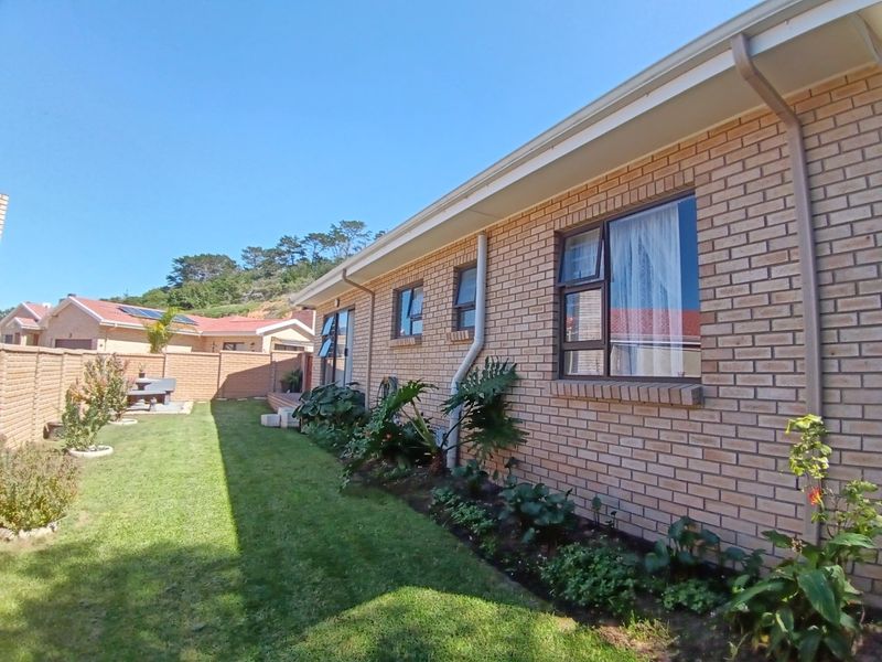 A view of the rear exterior of the house featuring face brick walls, aluminium window frames, and a well-maintained garden area.