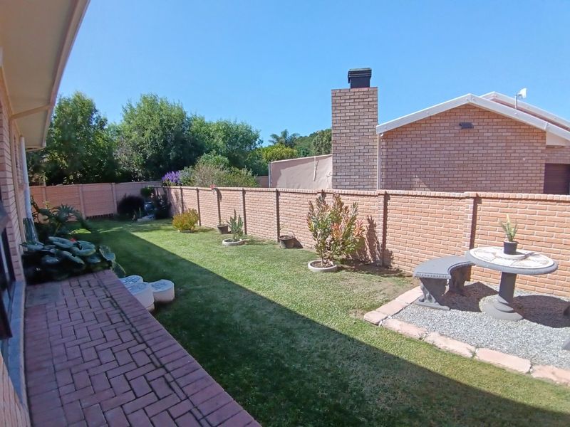 A well-maintained rear garden featuring a paved patio area, a brick boundary wall, and a prominent brick chimney stack.