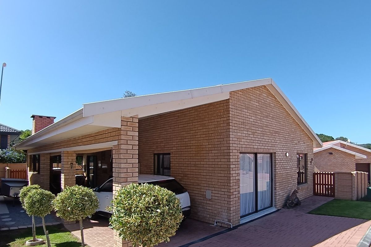 Rear view of a brick house featuring a covered patio area, paved driveway, and sliding glass door access to the interior.