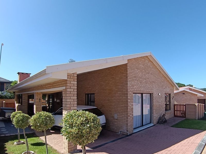 Rear view of a brick house featuring a covered patio area, paved driveway, and sliding glass door access to the interior.