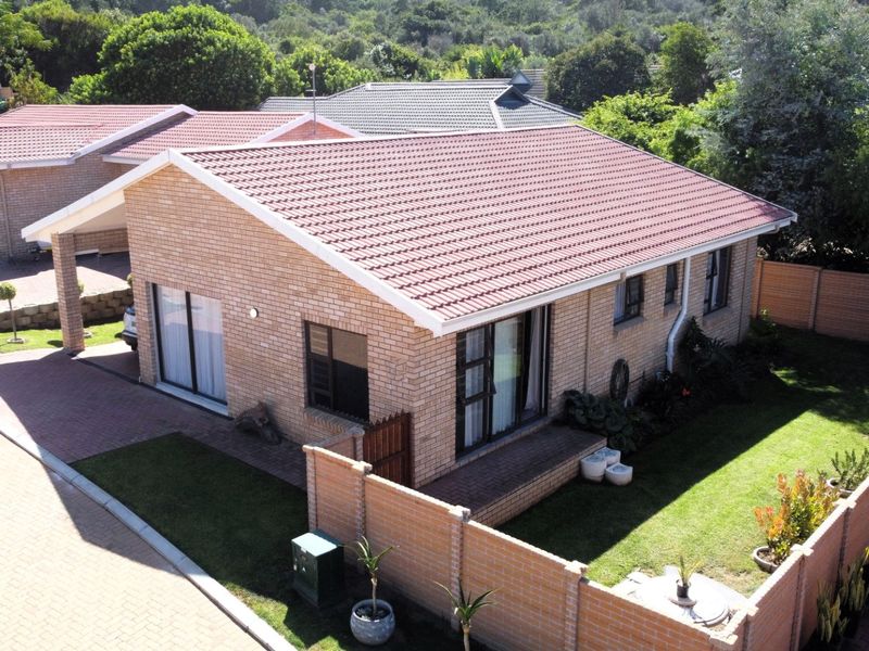 Aerial view of a well-maintained brick house featuring a tiled roof, paved driveway, covered carport, and a private garden with boundary walling.