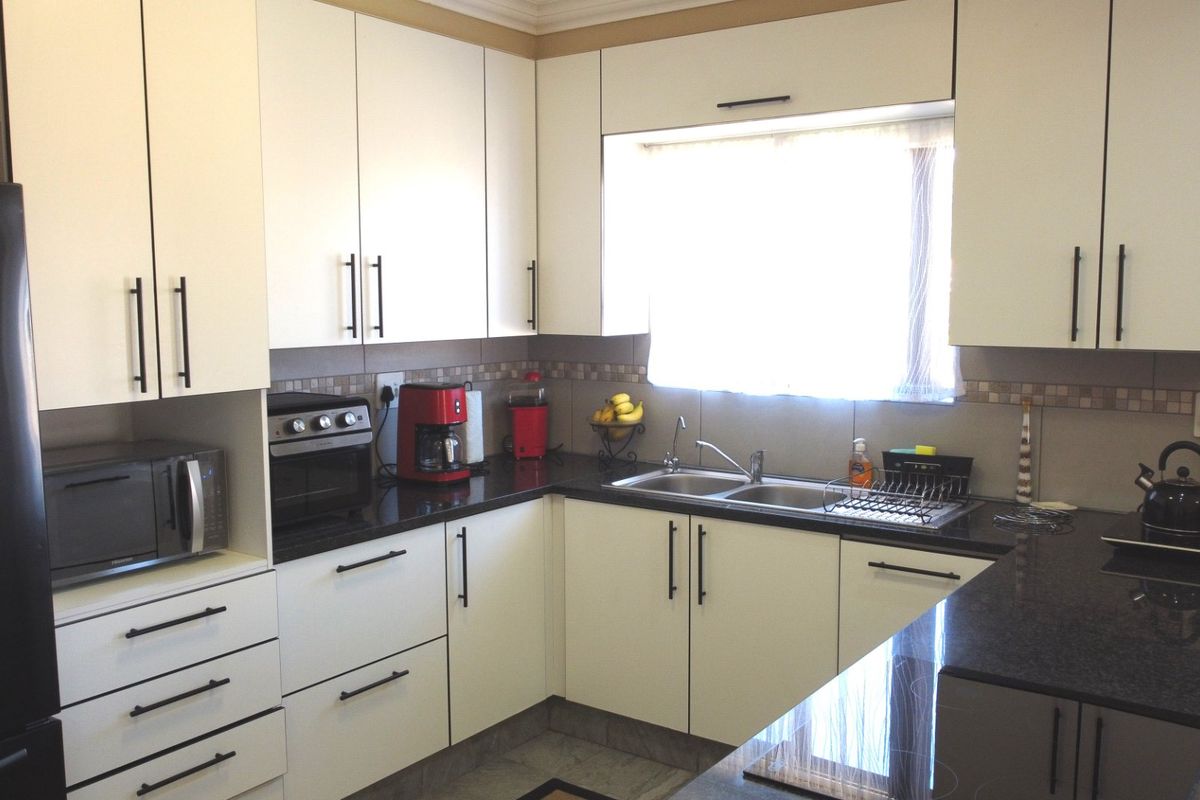 A functional kitchen featuring white cabinetry, dark granite countertops, a double basin sink, and a tiled backsplash with integrated oven.