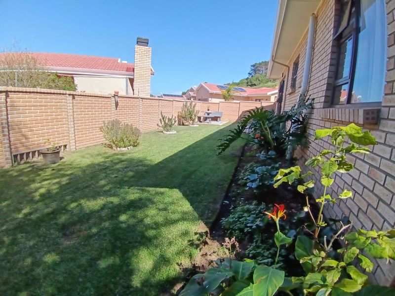A well-maintained rear garden featuring a neat lawn, established garden beds, and a solid brick boundary wall along the side of the house.