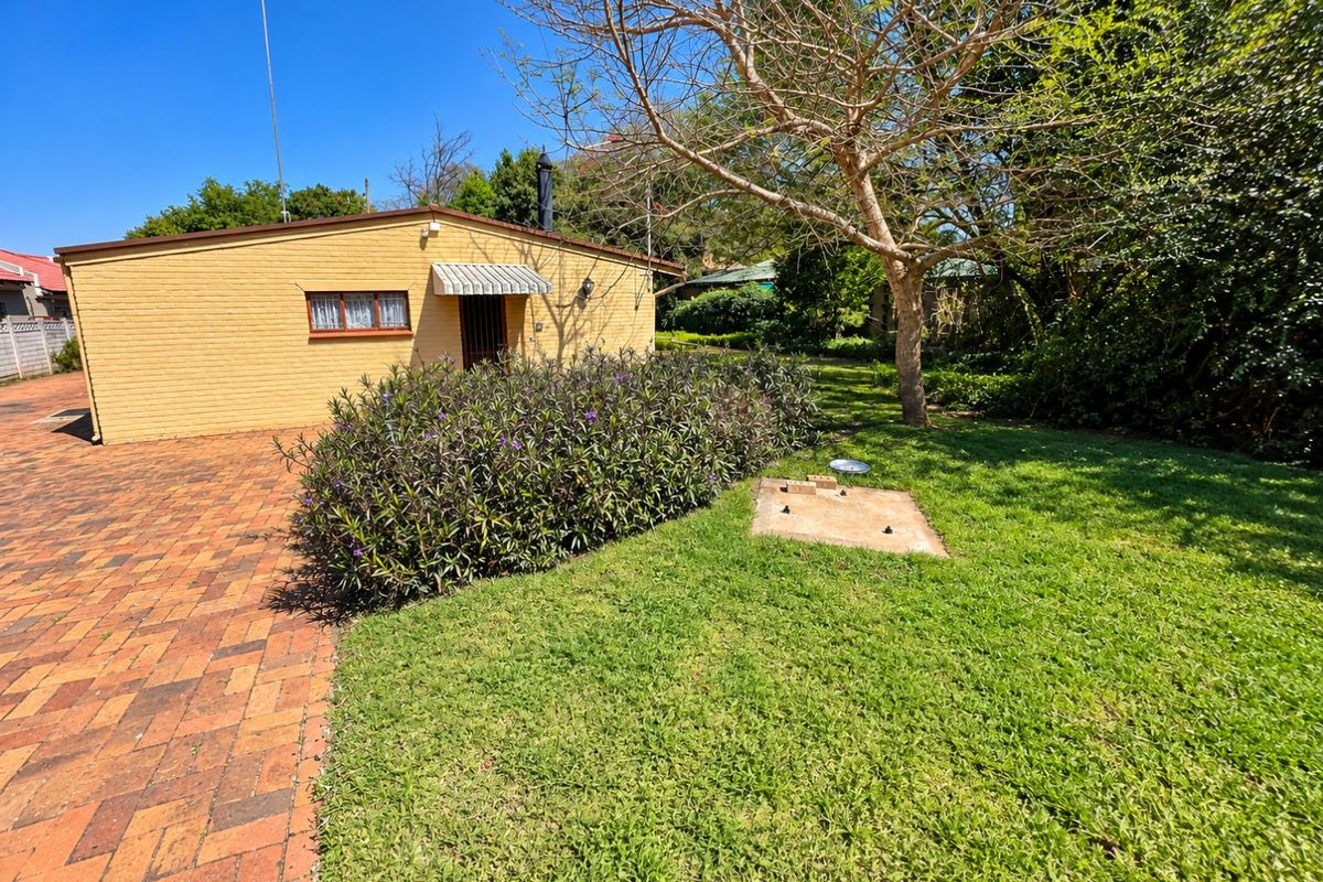 Rear view of the property featuring a brick facade, paved driveway area, and a well-maintained garden lawn.