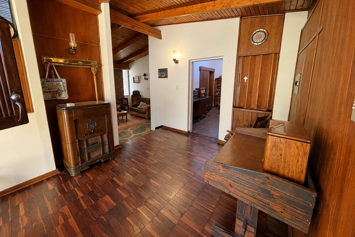 A living area featuring warm timber wall paneling, exposed ceiling beams, and classic parquet flooring, leading into an adjacent room.