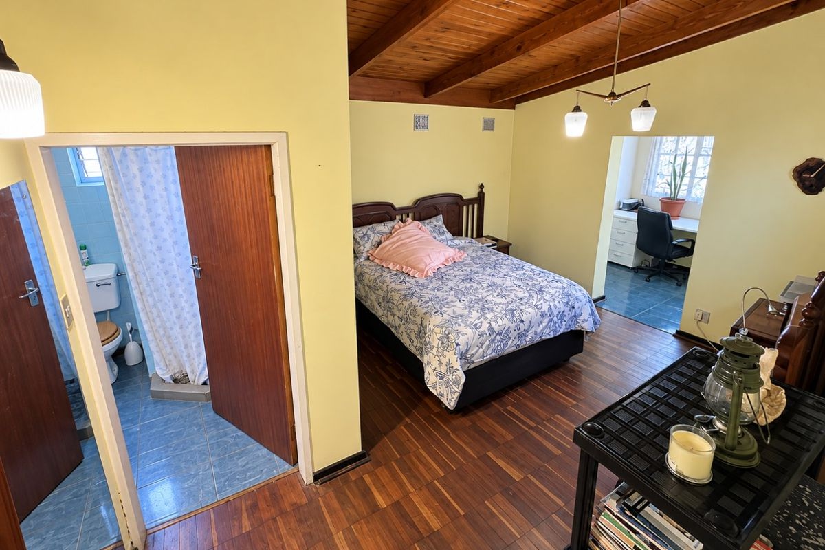 Spacious bedroom featuring exposed timber beam ceilings, parquet flooring, an en-suite bathroom, and an adjoining study area.