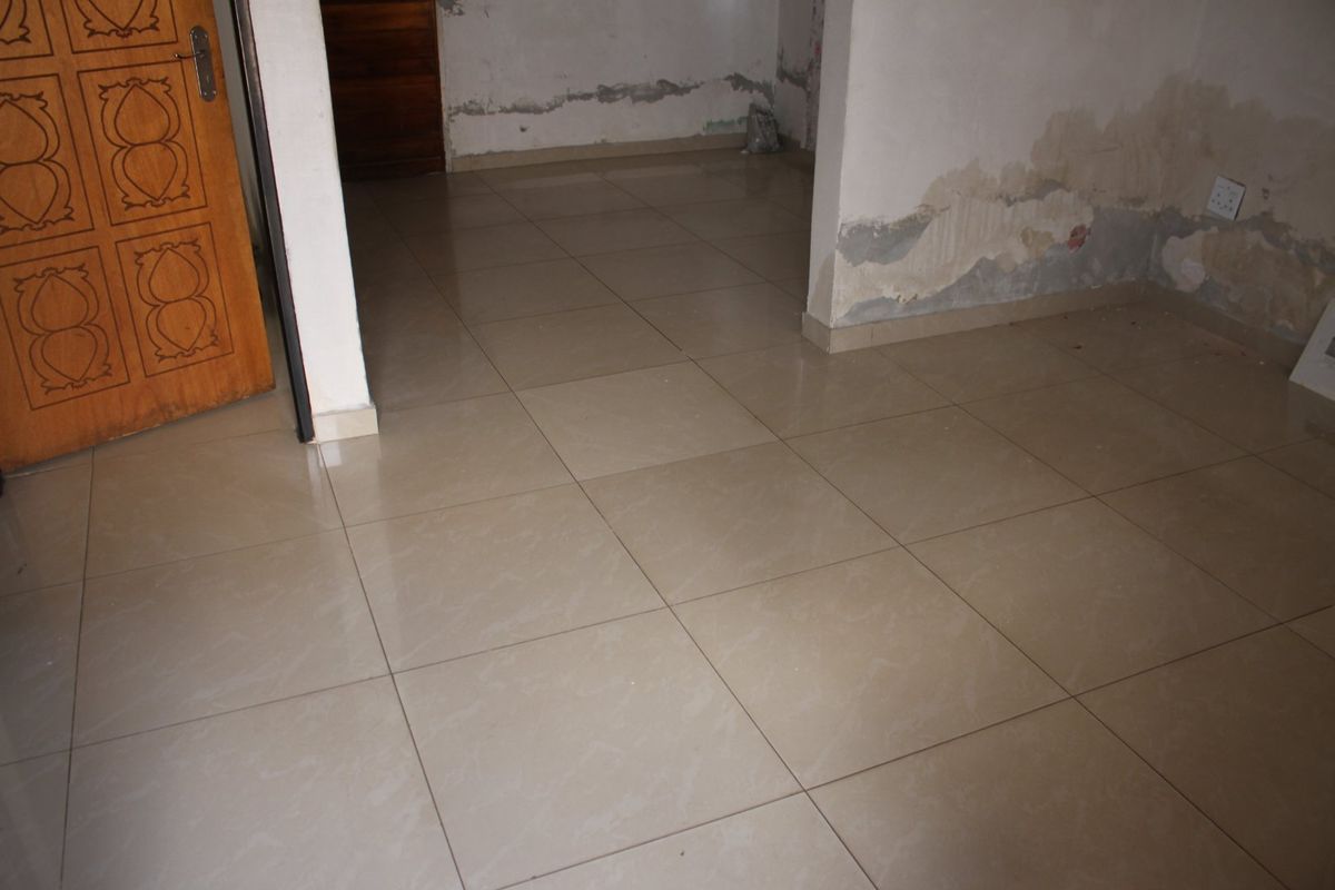 An empty living area featuring tiled flooring and a timber door, currently requiring wall repairs and repainting to restore the space.