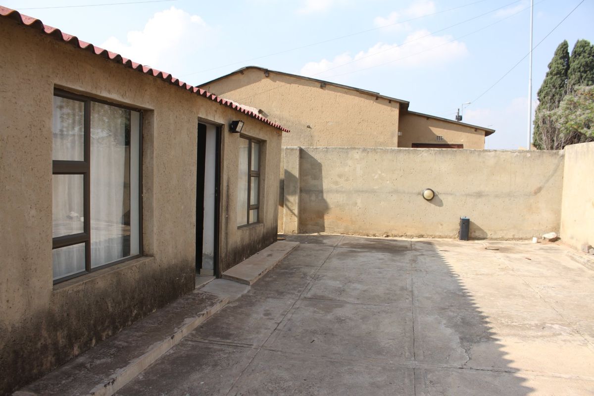 Rear exterior view of the property featuring a concrete paved courtyard, boundary wall, and basic building structure with aluminium window frames.