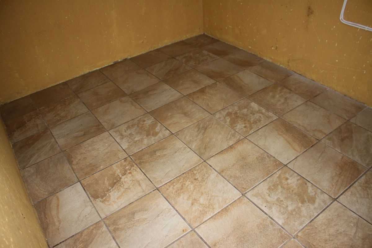 An empty corner space featuring brown ceramic floor tiles and yellow painted walls with visible surface wear.