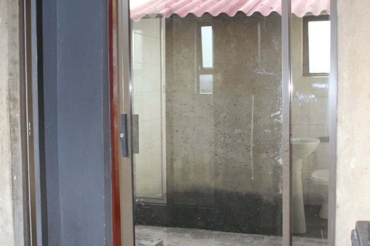 A view through a sliding glass door into an unfinished utility or bathroom area with exposed walls and basic sanitary fixtures.