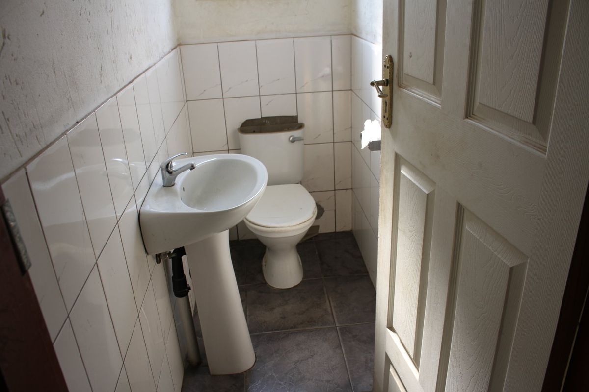 A small, dated bathroom featuring a pedestal basin and toilet with tiled finishes, currently requiring cosmetic updates and repairs.