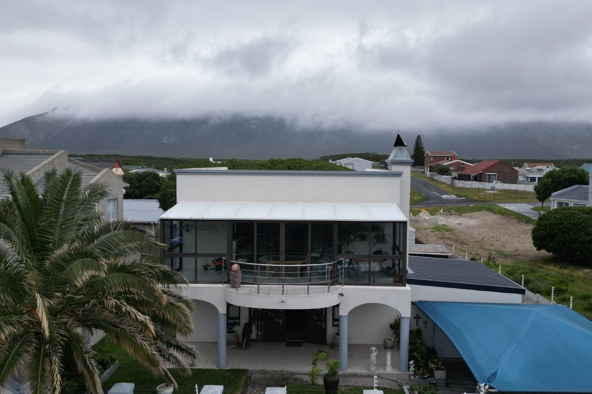 Aerial view of a two-story residential property featuring a balcony, covered patio, carport, and landscaped garden with perimeter security fencing.