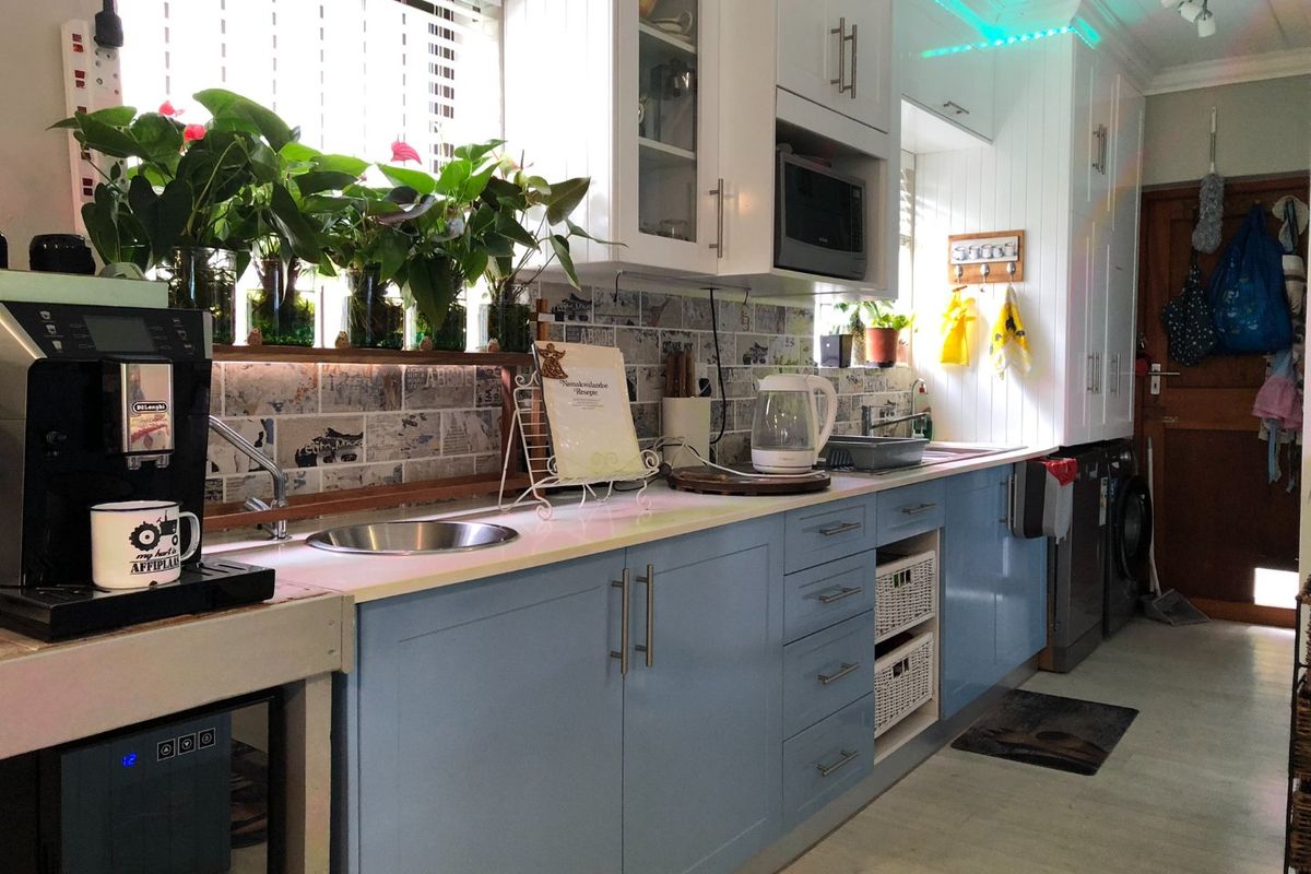 A functional kitchen featuring light blue cabinetry, a tiled backsplash, built-in microwave, and a stainless steel sink with ample counter space.