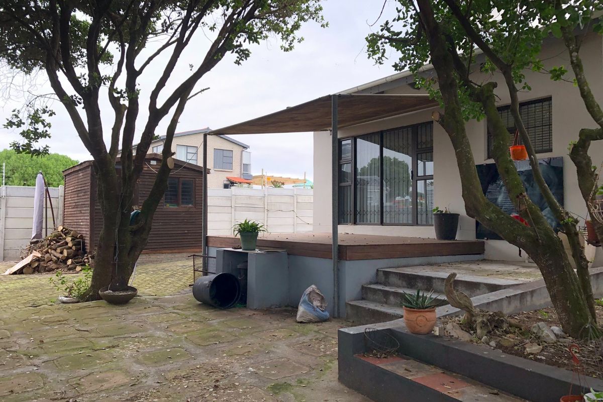 Rear exterior view featuring a timber deck, paved patio area, concrete steps, and a detached timber shed in the garden.