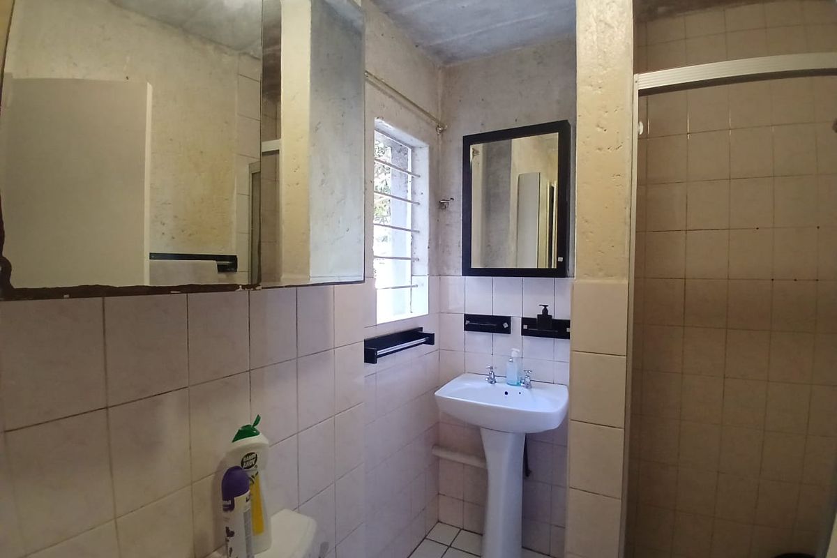 A dated bathroom featuring a pedestal basin, shower enclosure, and tiled finishes, requiring cosmetic updates to improve its overall condition and appeal.