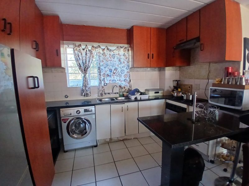 Functional kitchen featuring wood-tone cabinetry, granite countertops, tiled backsplash, and integrated laundry space, offering a practical layout for daily use.