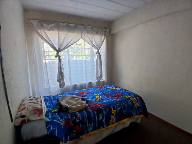 A compact bedroom featuring security bars on the window and basic finishes, requiring cosmetic updates to improve its overall appeal.