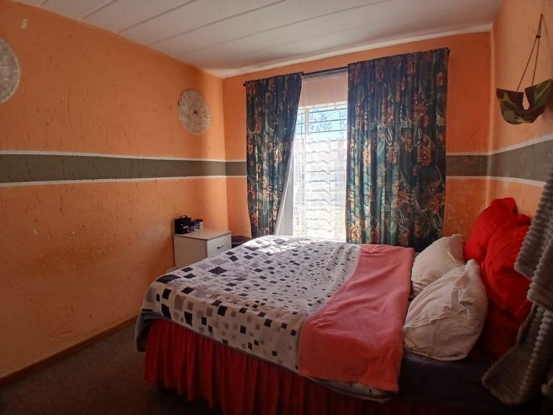 A bedroom featuring carpeted flooring and a window fitted with security bars, currently finished with textured orange wall paint.