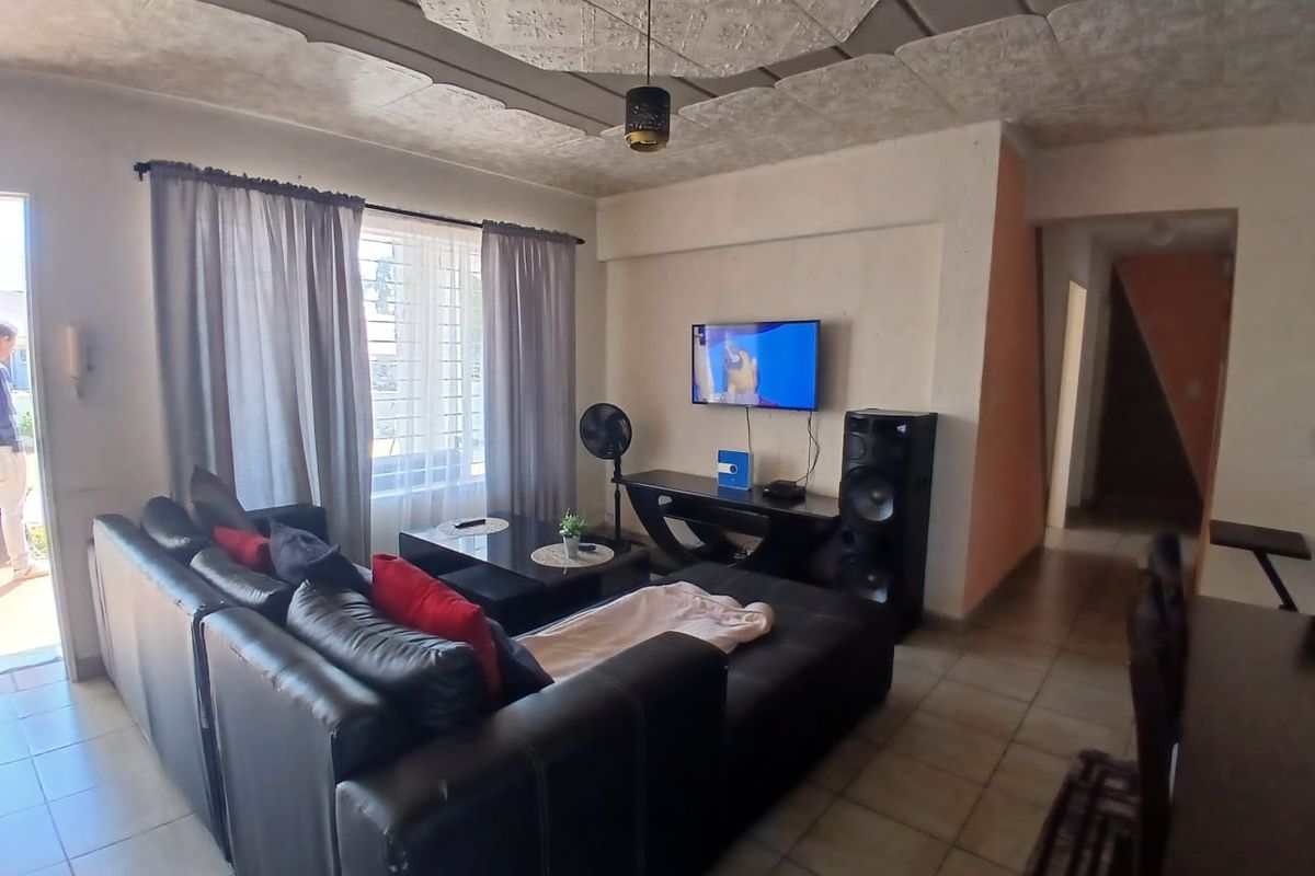 A living room featuring tiled flooring, a textured ceiling, and natural light through a window with security bars.