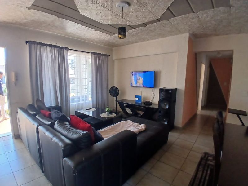 A living room featuring tiled flooring, a textured ceiling, and natural light through a window with security bars.