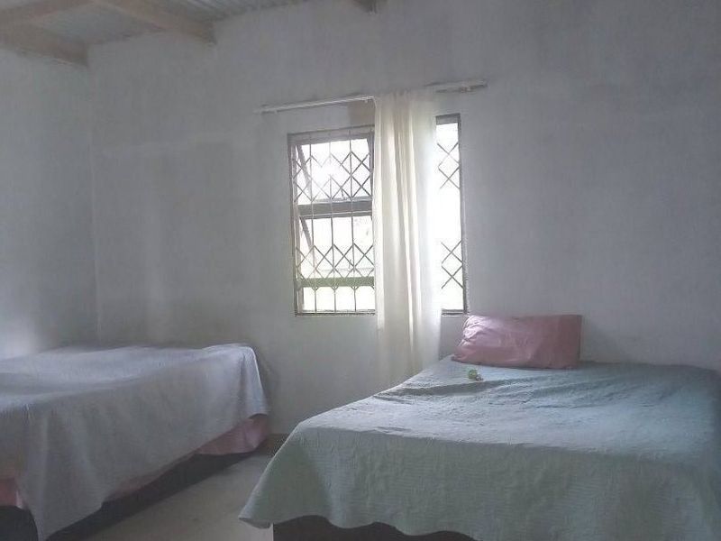 A bedroom featuring tiled flooring, a window with security bars, and an exposed corrugated metal ceiling structure.