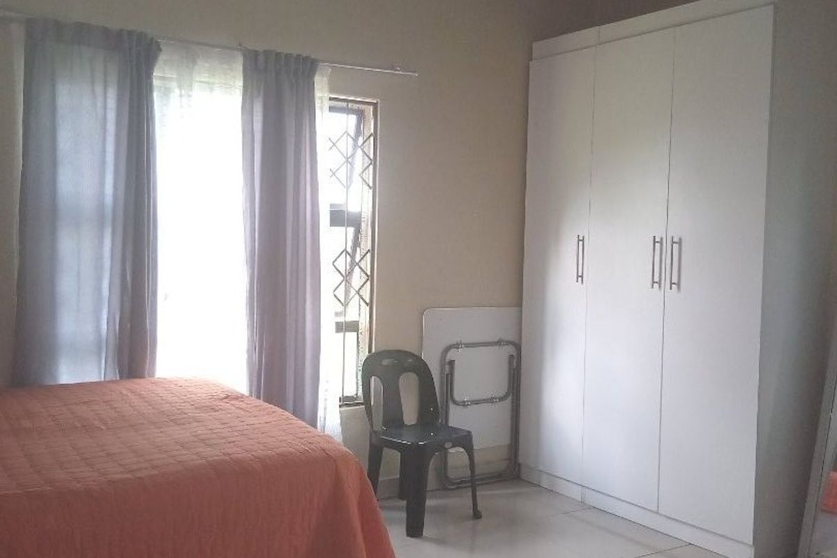 A bedroom featuring tiled flooring, a built-in wardrobe, and an exposed corrugated metal ceiling structure.