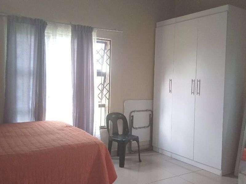 A bedroom featuring tiled flooring, a built-in wardrobe, and an exposed corrugated metal ceiling structure.