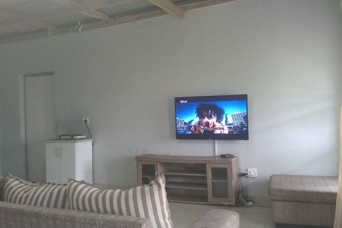 Living room featuring tiled floors and an exposed timber and corrugated metal ceiling, providing a basic, functional space ready for aesthetic updates.