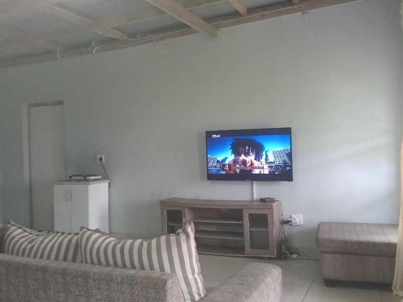 Living room featuring tiled floors and an exposed timber and corrugated metal ceiling, providing a basic, functional space ready for aesthetic updates.