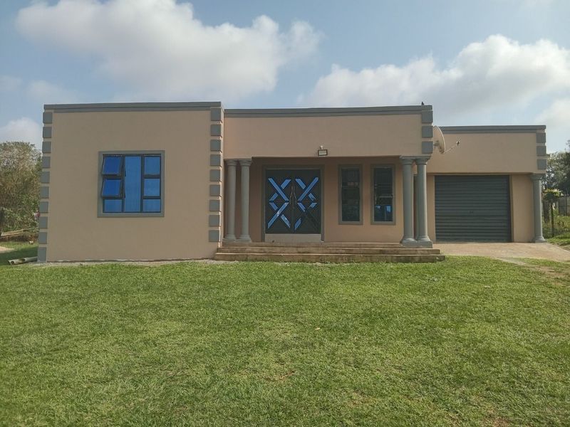 Front elevation of a single-story residential property featuring a paved entrance with decorative columns, a roller garage door, and a well-maintained lawn.