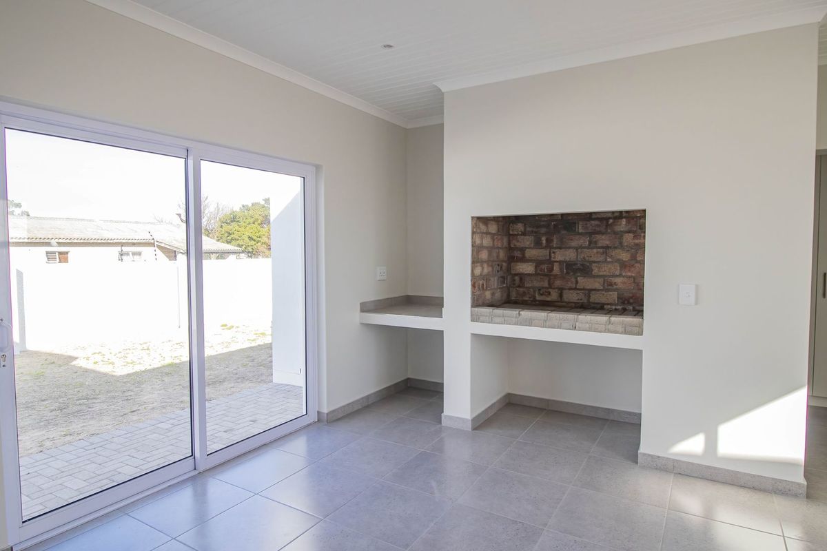 Bright living area featuring a built-in brick braai, tiled flooring, and large sliding glass doors providing direct access to the outdoor space.