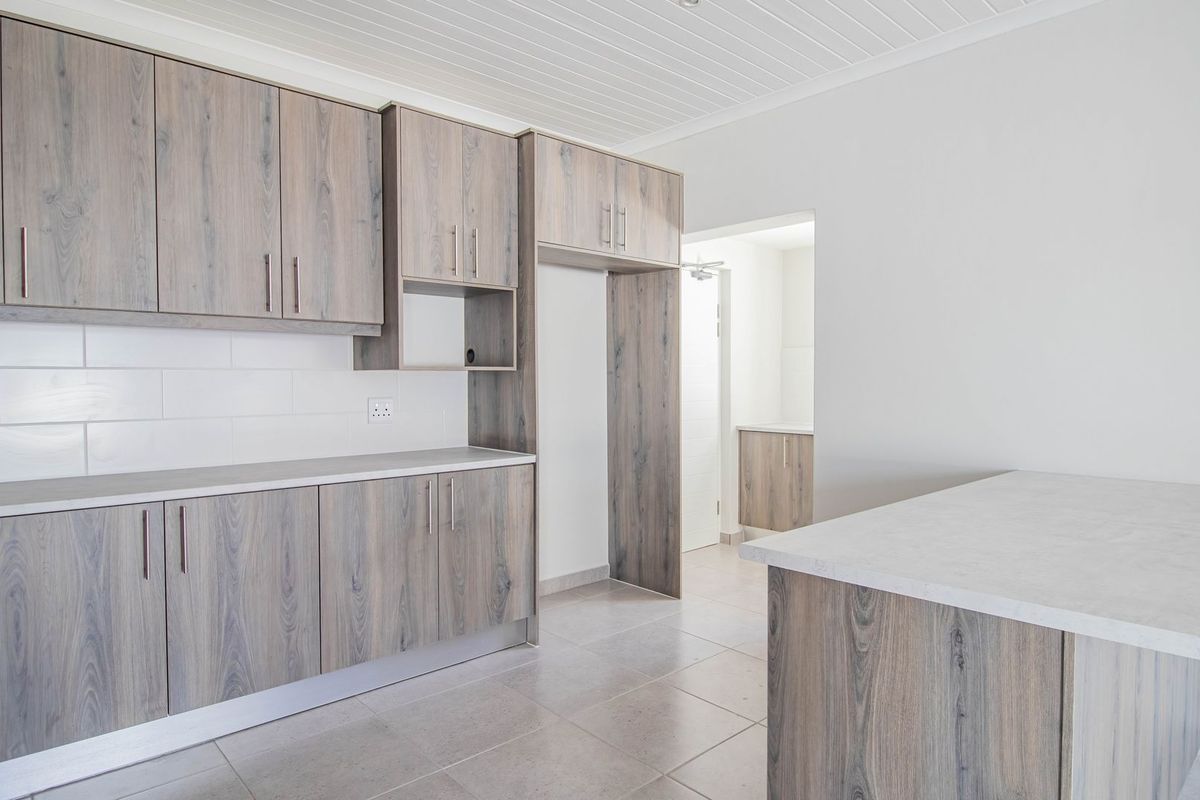 Modern kitchen featuring light wood-grain cabinetry, stone-look countertops, white tiled backsplash, and neutral floor tiles in an open-plan layout.