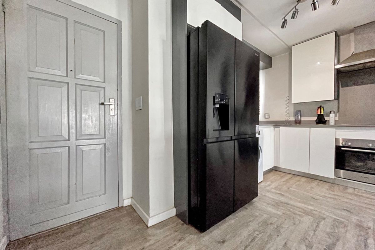 A modern kitchen featuring sleek white cabinetry, a built-in oven with extractor fan, and durable laminate flooring, offering a clean and functional workspace.