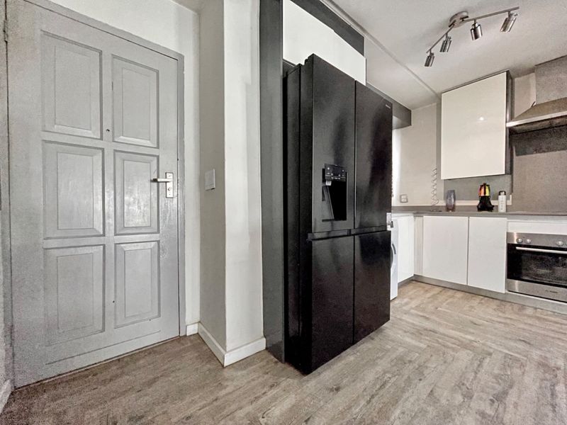 A modern kitchen featuring sleek white cabinetry, a built-in oven with extractor fan, and durable laminate flooring, offering a clean and functional workspace.