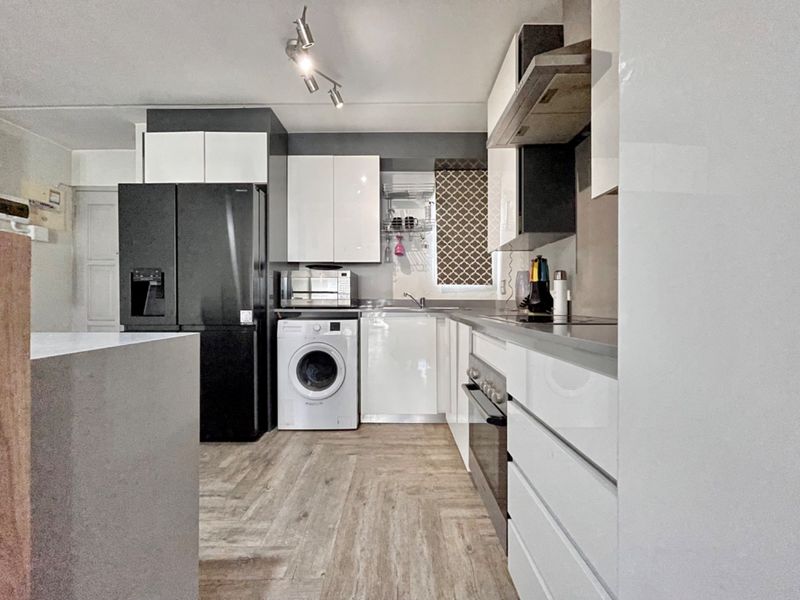 Modern kitchen featuring sleek white and dark cabinetry, integrated appliances, stainless steel oven, extractor fan, and durable wood-look laminate flooring.