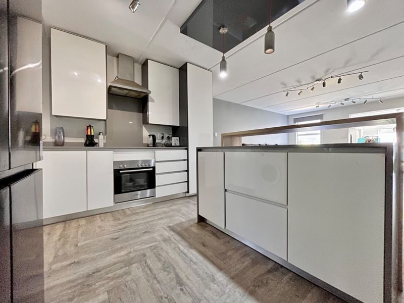 Modern open-plan kitchen featuring a central island, sleek white cabinetry, built-in oven, extractor fan, and durable wood-look laminate flooring.