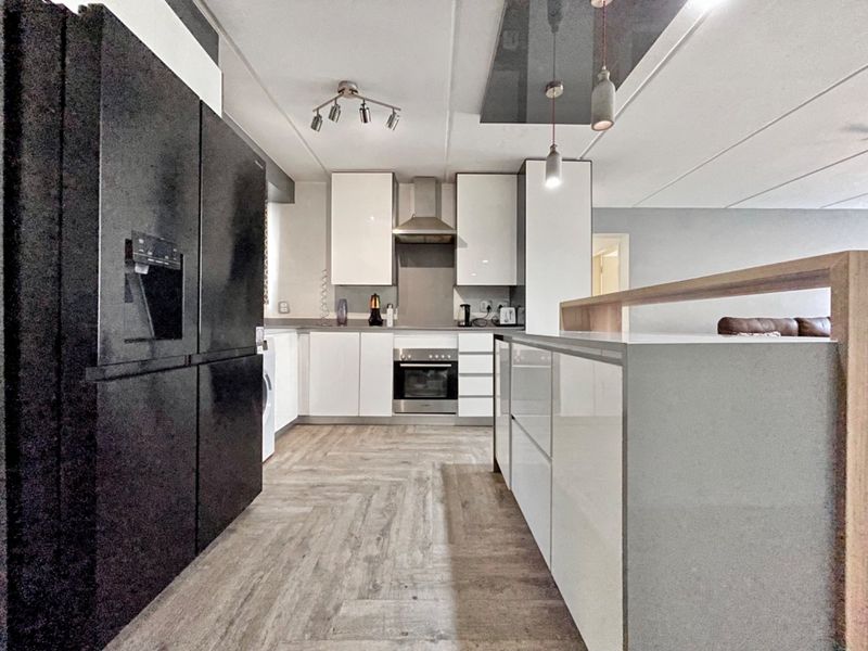 Modern kitchen featuring sleek white cabinetry, a central island, built-in oven, extractor fan, and durable herringbone-style laminate flooring.
