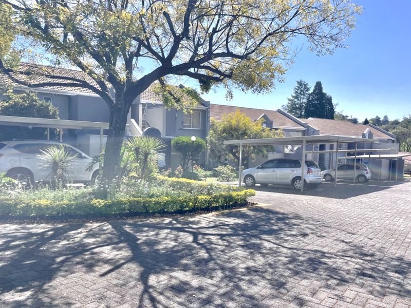 Front exterior view of the townhouse complex featuring paved driveway, covered carports, and established garden landscaping.