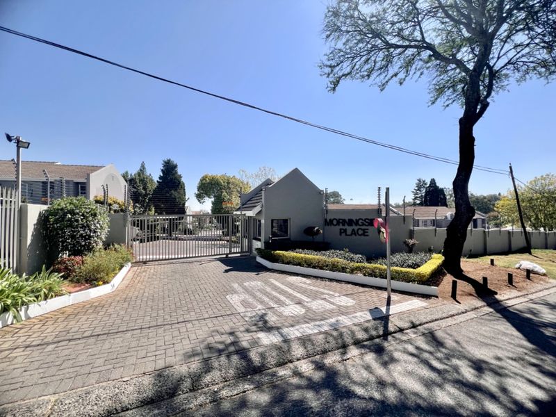 The secure entrance to Morningside Place townhouse complex, featuring a paved driveway, automated security gate, and perimeter wall with electric fencing.