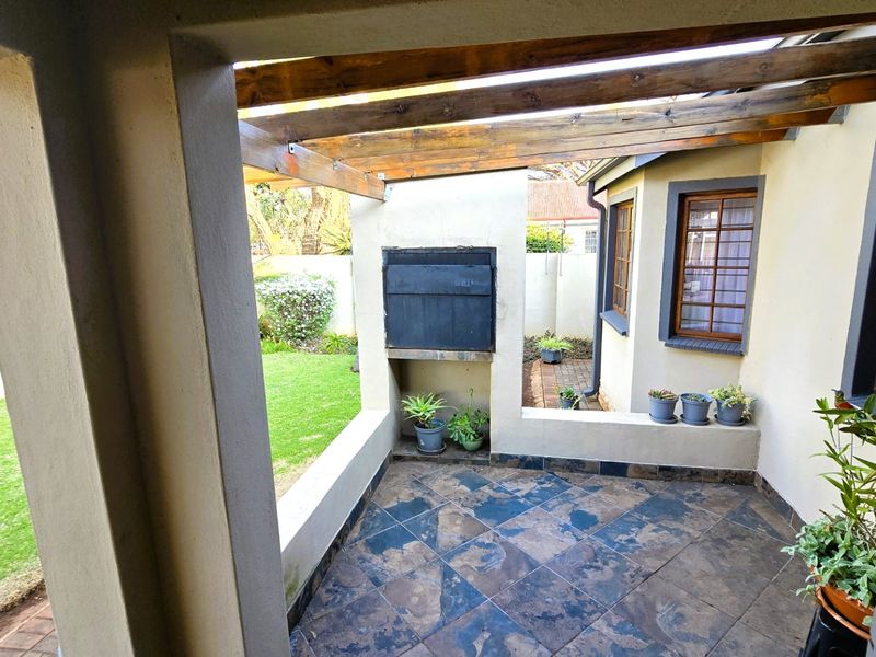 Covered patio area featuring a built-in braai, timber pergola structure, and tiled flooring, overlooking the rear garden.