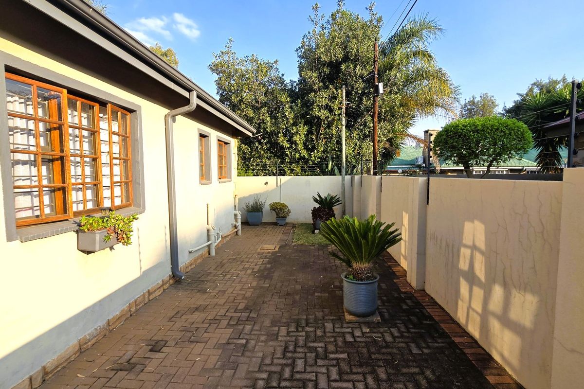 A paved rear courtyard area featuring a boundary wall and timber-framed windows, offering a private outdoor space with potential for landscaping improvements.