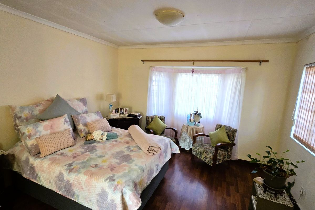 A spacious bedroom featuring warm laminate flooring, a large bay window with natural light, and neutral wall finishes.