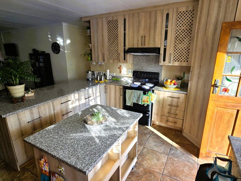 A functional kitchen featuring light wood-tone cabinetry, granite countertops, a freestanding stove with extractor, and durable tiled flooring.