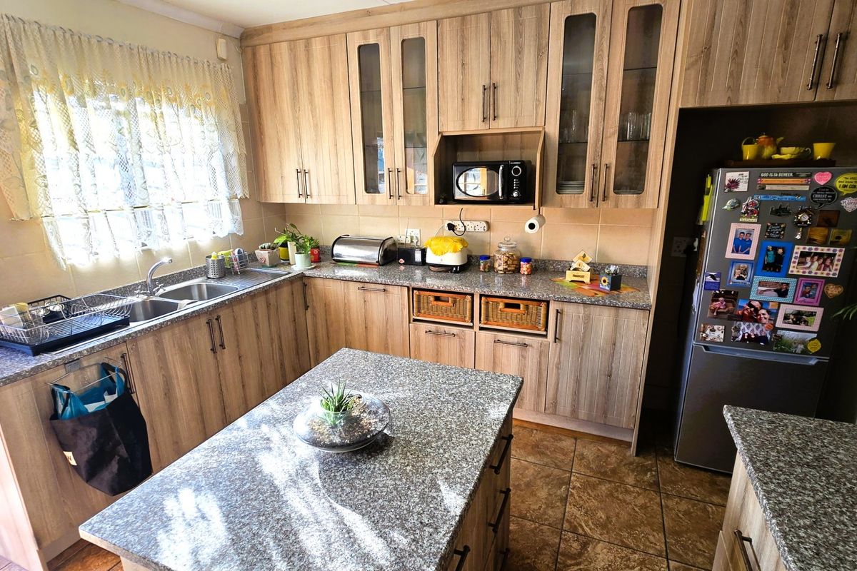 A functional kitchen featuring wood-look laminate cabinetry, granite countertops, a central island, and a double basin sink with tiled flooring.