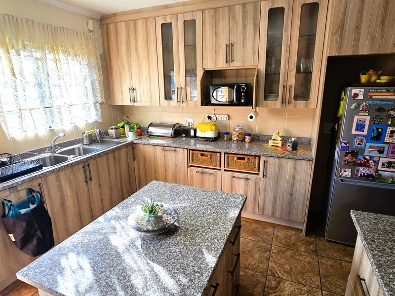 A functional kitchen featuring wood-look laminate cabinetry, granite countertops, a central island, and a double basin sink with tiled flooring.