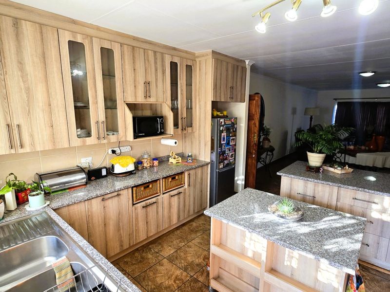 Open-plan kitchen featuring wood-look cabinetry, granite countertops, a central island, and tiled flooring, seamlessly flowing into the adjacent living area.
