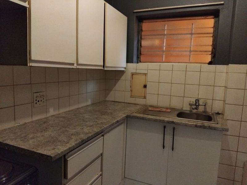 A compact kitchen featuring laminate countertops, a stainless steel sink, and white cabinetry with tiled splashbacks, ready for a modern update.