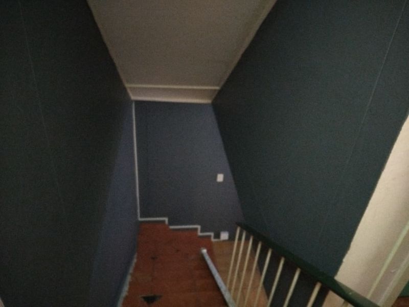A narrow interior hallway and staircase area featuring dark painted walls and exposed flooring in need of repair.